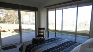 A bedroom with a large bed, a chair, and a view of a landscaped area outside.
