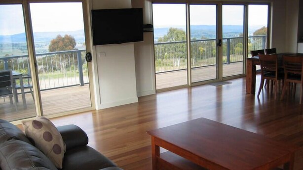 A spacious living area with a wooden coffee table, a leather sofa with patterned cushions, and a flat-screen TV mounted on the wall.