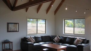 A spacious living room with a large sectional sofa, a wooden coffee table, and large windows offering views of a grassy field.