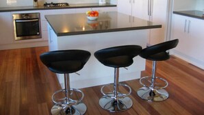 A modern kitchen with a central island, three bar stools, stainless steel appliances, and white cabinetry.