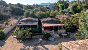 Una villa rústica con techo de tejas, rodeada de vegetación exuberante y un paisaje montañoso.