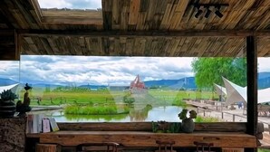 A rustic wooden bar with a view of a serene landscape including a pond, grassy fields, and distant mountains. - Caiyunjian Inn (Shangri-La)