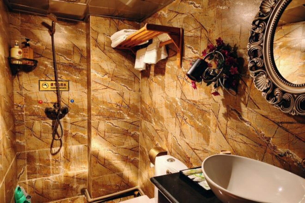 A bathroom with a marble wall, a shower, a sink, a mirror, and a towel rack.