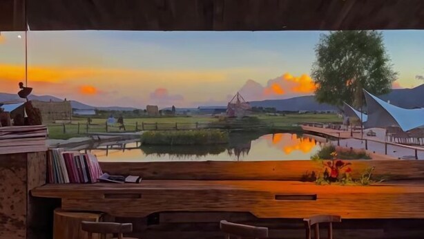 A bar area with a view of a sunset landscape, including a body of water, trees, and distant mountains. - Caiyunjian Inn (Shangri-La)