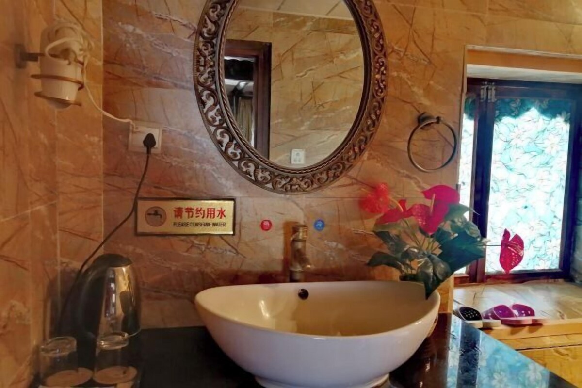 A bathroom with a large oval sink, a mirror with an ornate frame, a towel ring, and a sign indicating the use of water.