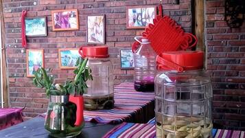 A table with jars containing various items, a brick wall with framed pictures, and a red object on the wall.