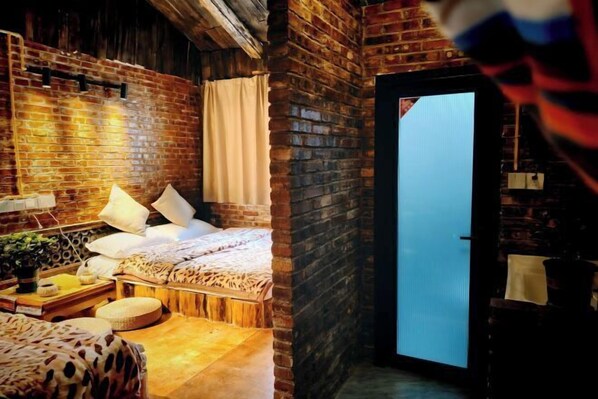 A cozy room with a brick wall, a bed with white bedding, a wooden bench, and a small table with a plant. - Caiyunjian Inn (Shangri-La)