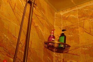 A bathroom with a marble wall, a showerhead, and a metal shelf holding toiletries. - Caiyunjian Inn (Shangri-La)