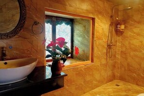 A bathroom with a large vessel sink, a mirror, a window with a view of red flowers, and a shower area. - Caiyunjian Inn (Shangri-La)