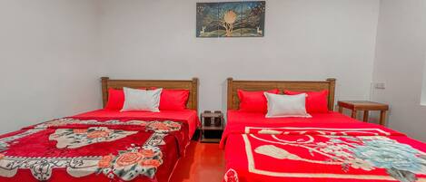 A room with two wooden beds, each with red bedding and floral patterns. There is a small wooden nightstand on each bed.