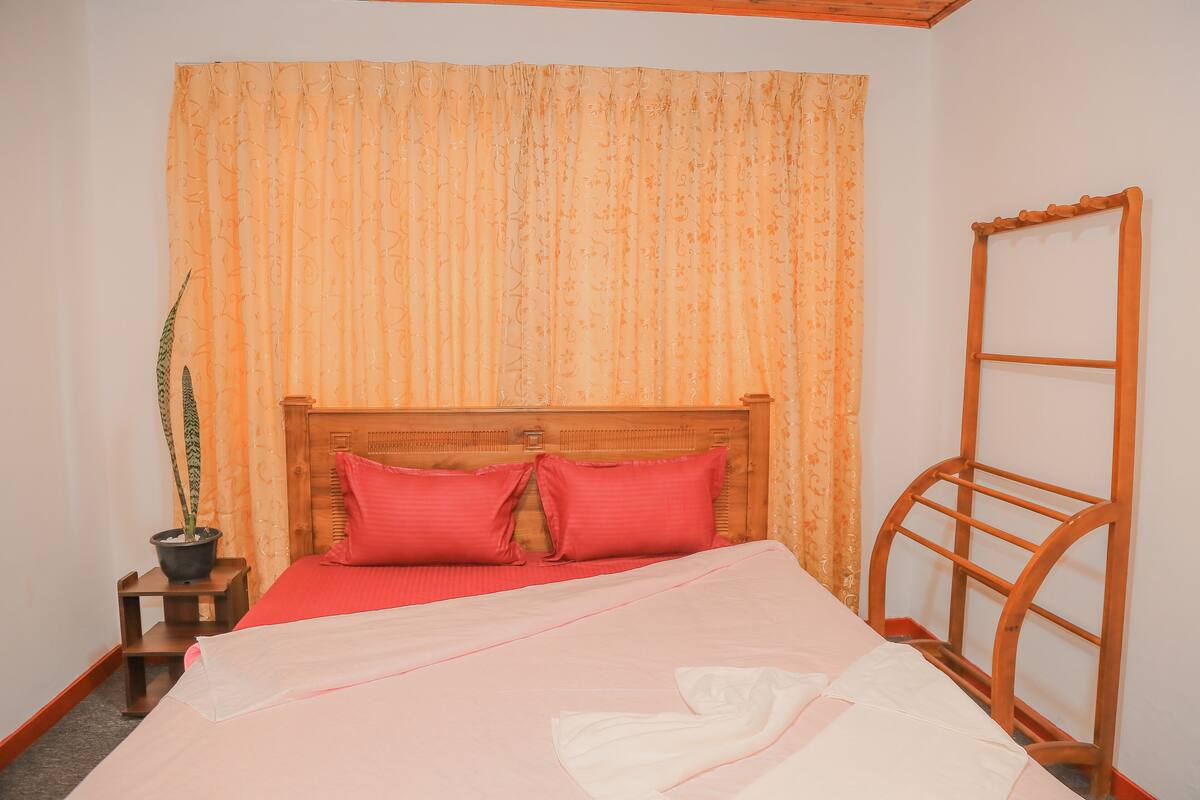 A neatly made bed with a wooden headboard, a small bedside table with a potted plant, and a wooden ladder against the wall.