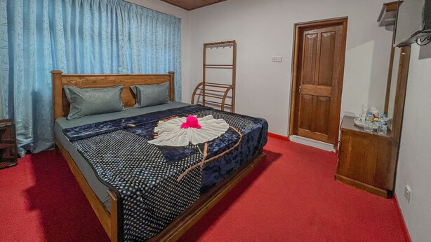 A bedroom with a wooden bed, a red carpet, a wooden wardrobe, and a mirror on the wall. - Royal Guest Inn (Nuwara Eliya)