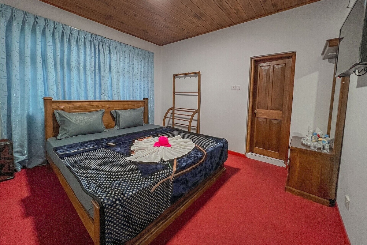 A bedroom with a wooden bed, a red carpet, a wooden wardrobe, and a mirror.