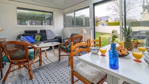 Quarto iluminado pelo sol, com sofá, cadeiras, mesa e vista para o exterior.