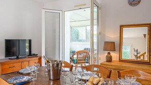 Uma sala de jantar com uma mesa de madeira posta para refeição, uma televisão sobre um suporte e um espelho grande na parede.