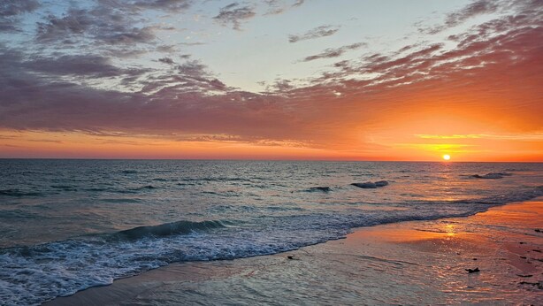 Une plage avec des vagues, un coucher de soleil et un ciel dégagé.