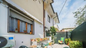 Une petite terrasse avec une table et des chaises, une fenêtre avec des rideaux et des plantes en pot.