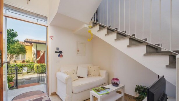 Un salon moderne avec un canapé blanc, une petite table basse, un téléviseur et un escalier.