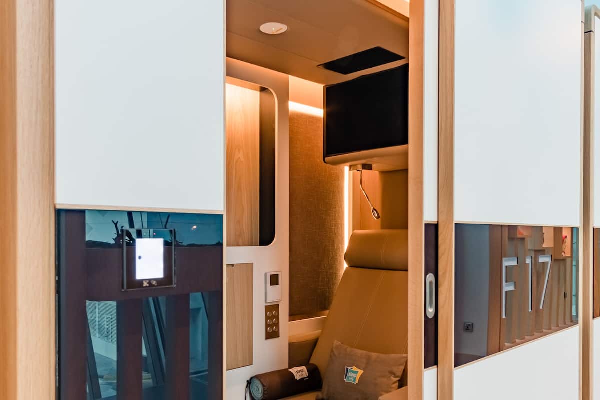 A compact, modern room with a sliding door, a bed, a small seating area, and a mounted television.