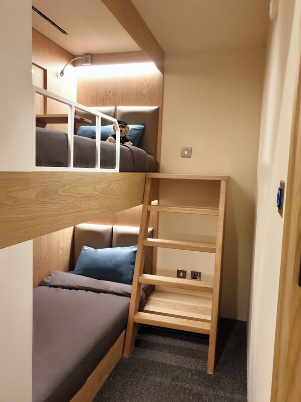 Un lit superposé avec une échelle en bois, une petite étagère et un luminaire au-dessus.