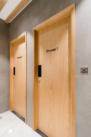 Two wooden shower doors labeled "Shower 1" and "Shower 2" in a modern bathroom with a grey tiled floor and a ceiling with wooden beams.