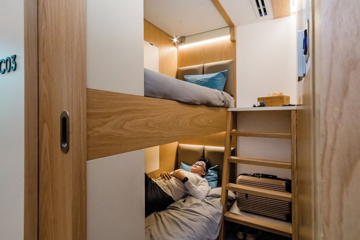A compact, modern room with a bunk bed, wooden shelving, and a small desk area.