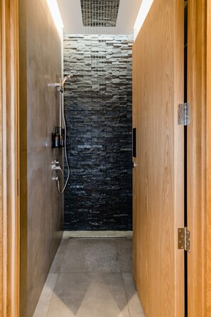 A modern shower area with a stone wall, wooden door, and a metal showerhead.