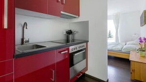 Una cocina compacta con armarios rojos, un lavamanos de acero inoxidable y un horno.