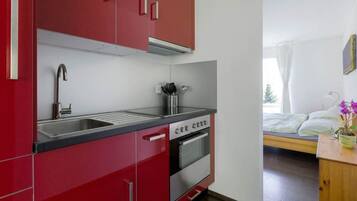Une cuisine de taille réduite avec des meubles de rangement rouges, un évier en acier inoxydable et un four.