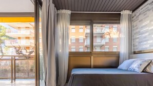 Une chambre d’hôtel moderne dotée d’un grand lit, offrant une vue sur le paysage urbain à travers une grande fenêtre, et d’un balcon avec vue sur les bâtiments environnants.