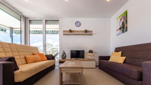 A modern living room with two sofas, a coffee table, a TV, and a small shelf with decorative items. - Acantilados by Interhome (Salou)