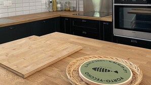 Una cucina moderna con mobili neri, un piano di lavoro in legno ed elettrodomestici in acciaio inossidabile, tra cui una cappa aspirante e forni.