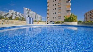 Ein Schwimmbad mit klarem, blauem Wasser, umgeben von modernen Gebäuden mit Balkonen und einer Steinmauer.