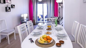 Een eethoek met een tafel voor vier personen, stoelen, een televisie en uitzicht buiten door een raam met strepen gordijnen.