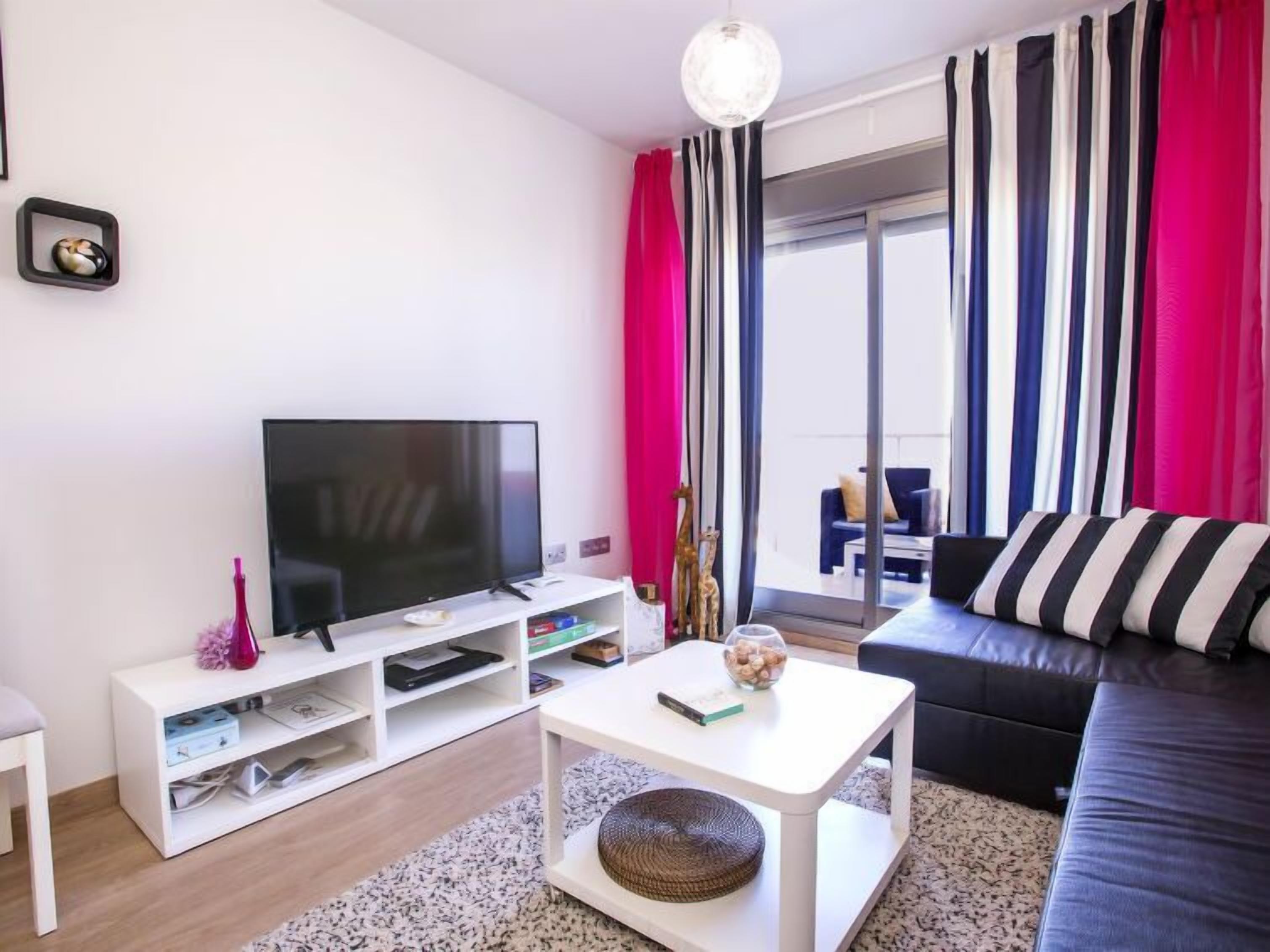 Uma sala de estar moderna com televisão de tela plana, console branco e sofá de couro preto.