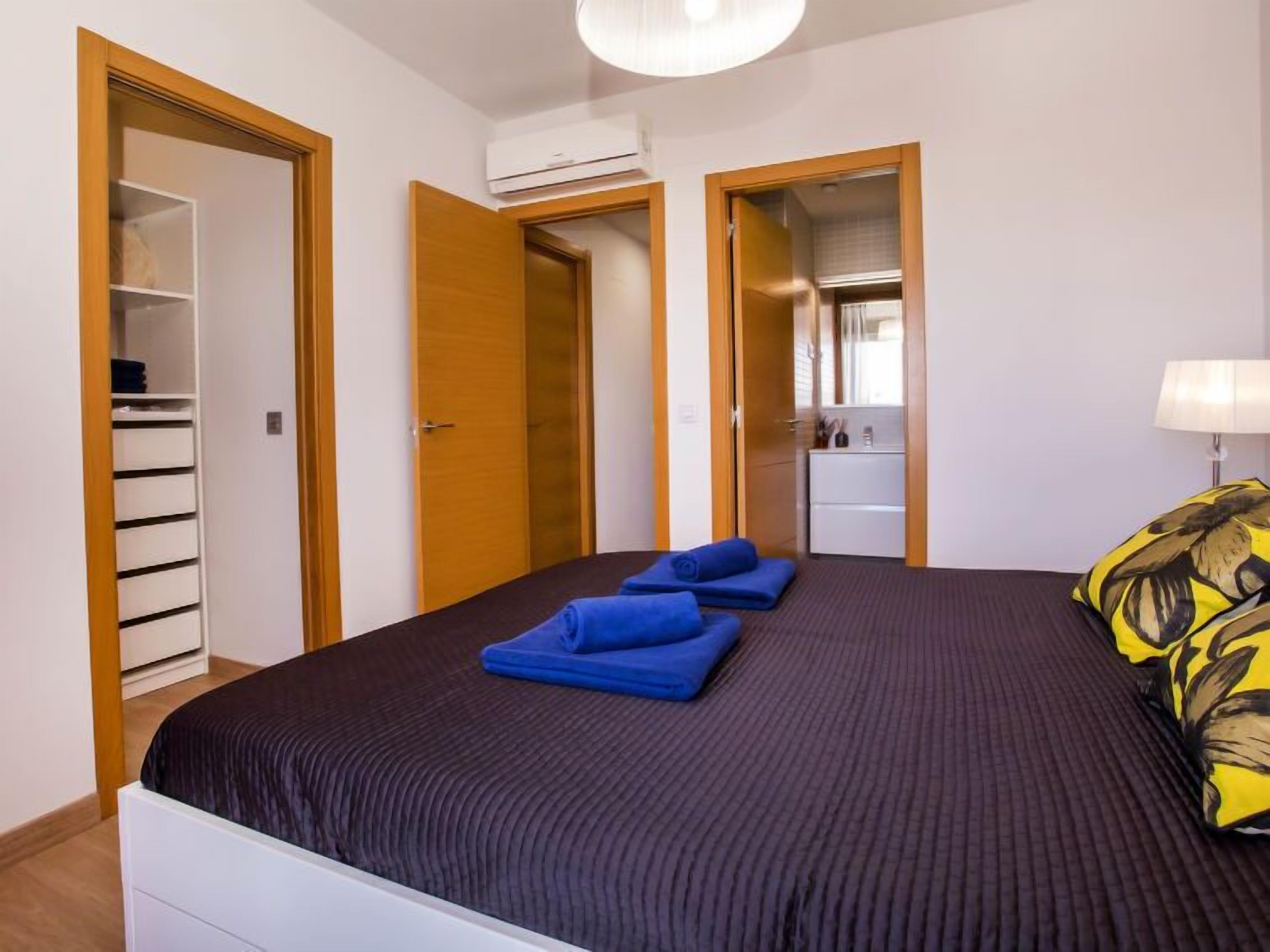 Un dormitorio con cama, armario, espejo y mesita de noche.
