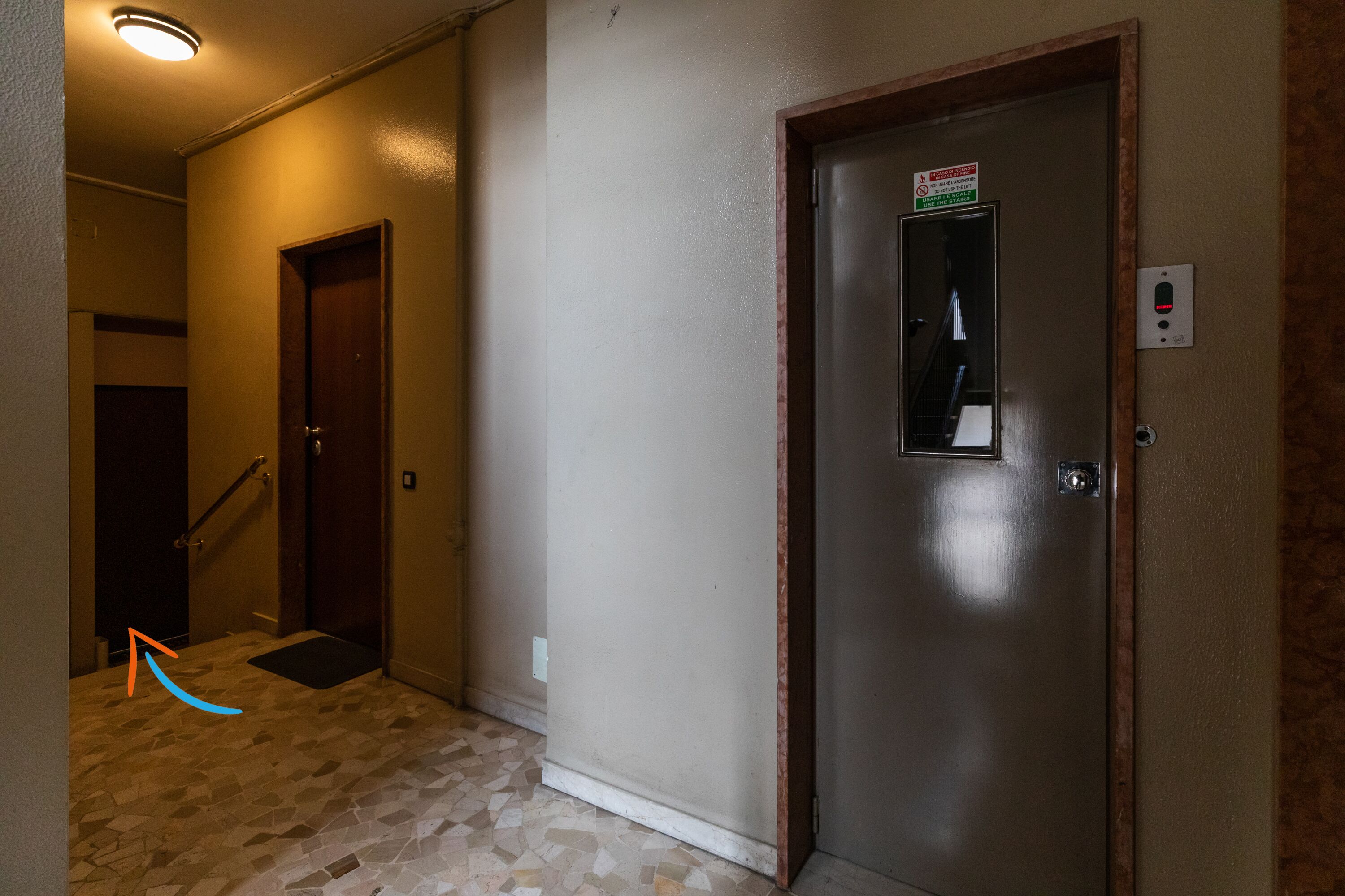 Un couloir avec un sol carrelé, une porte avec une pancarte et un luminaire au plafond.