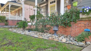 A house with a porch, a brick wall, and a garden with rocks and plants. - Emma’s Cottage (Montgomery)