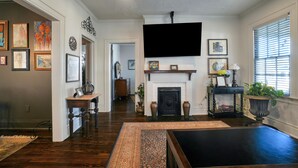 A living room with hardwood flooring, a fireplace, a mounted flat-screen TV, and a variety of framed artwork on the walls. - Emma’s Cottage (Montgomery)