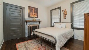 A bedroom with a bed, a fireplace, a door, and a window with blinds. - Emma’s Cottage (Montgomery)