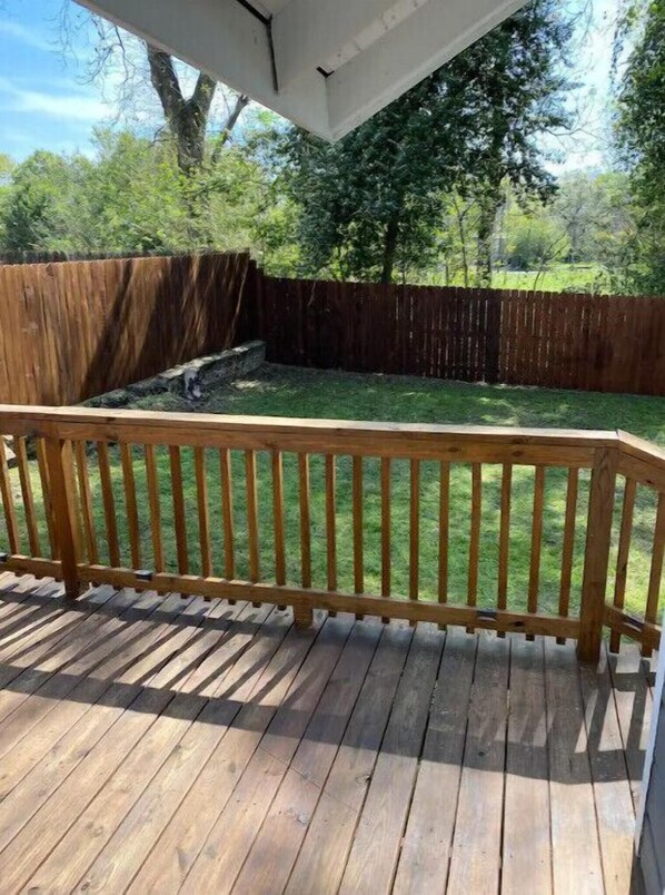 A wooden deck with a railing, surrounded by a wooden fence and a grassy yard.
