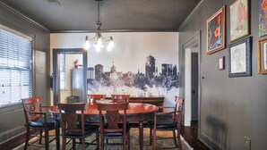 A dining room with a round table and chairs, a chandelier, and a cityscape mural on the wall. - Emma’s Cottage (Montgomery)