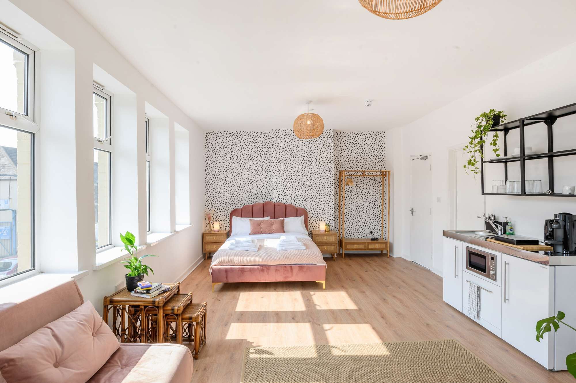 Ein modernes Schlafzimmer mit einem großen Bett, einem Nachttisch mit Lampe, einem Kleiderschrank und einer Küchenzeile inklusive Kaffeemaschine.