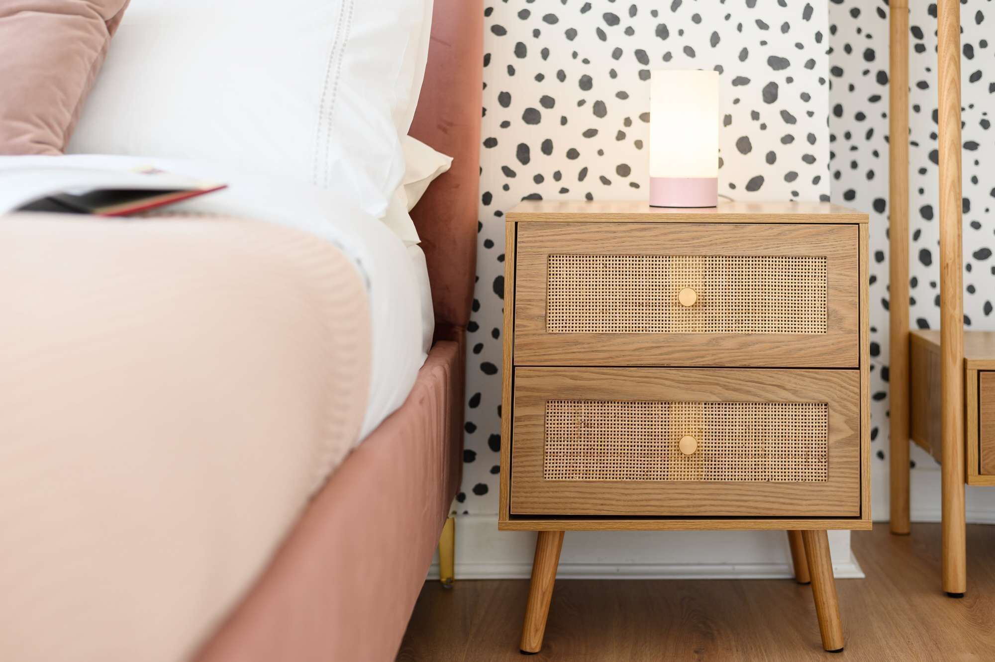 A bedroom with a bed, a bedside table with a lamp, and a polka dot wallpaper.