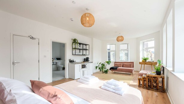 Ein modernes Schlafzimmer mit einem großen Bett, einer Sitzecke mit einer Couch und einer Küche im Hintergrund.