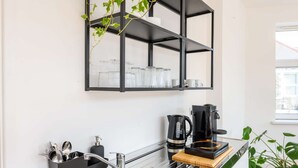 Eine moderne Küche mit einem schwarzen Metallregal, das Glaswaren, eine Kaffeemaschine und eine Spüle mit Besteck beherbergt.