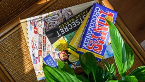 Ein Korbtablett mit verschiedenen Gegenständen, darunter ein Buch, eine Schokoladentafel und einige Blätter Papier.