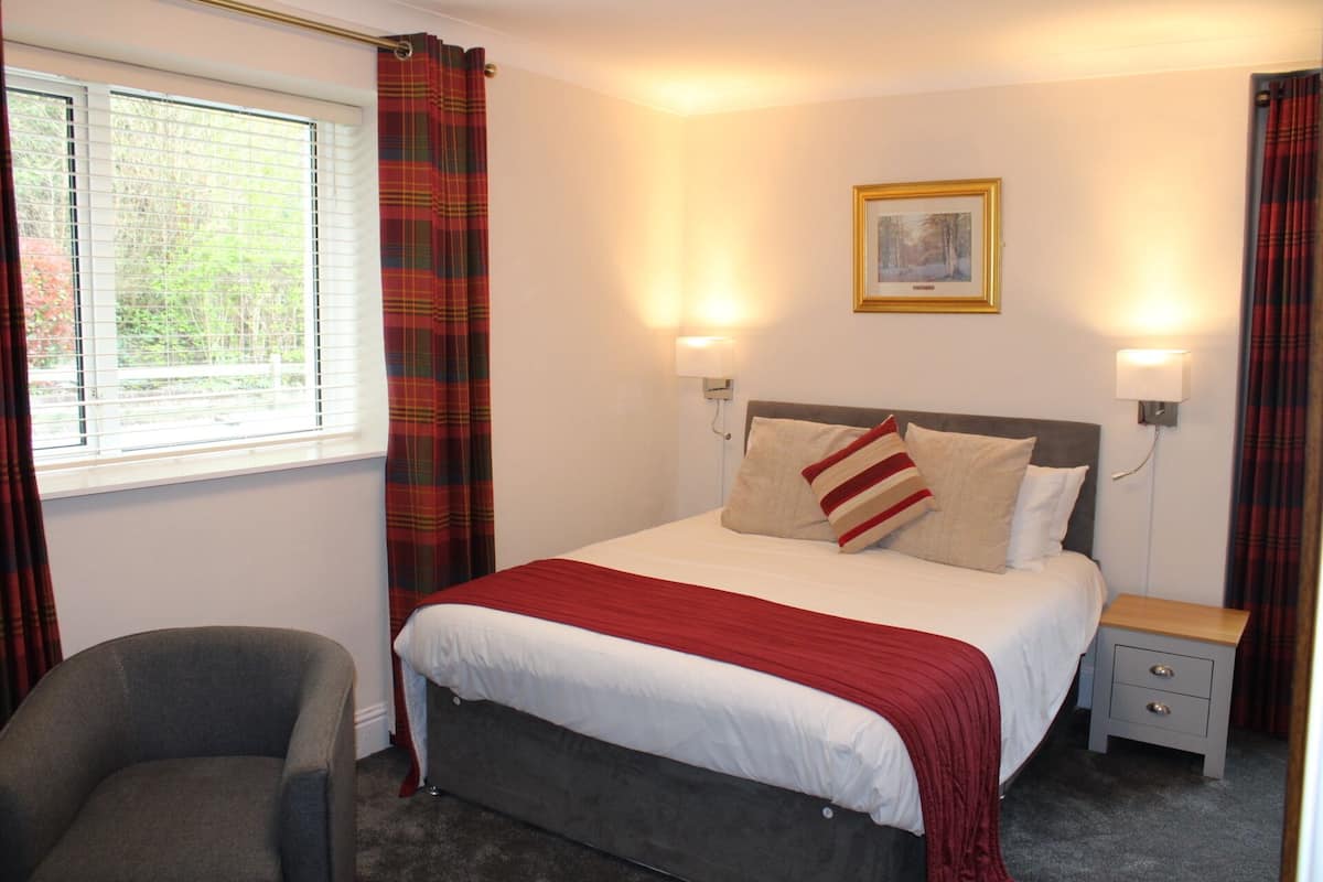 A neatly arranged bedroom with a bed, bedside tables, a chair, and a window with curtains.