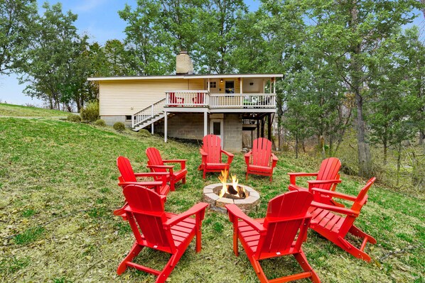 A house with a deck and a fire pit surrounded by red Adirondack chairs.