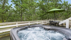 Ein Whirlpool auf einer Holterrasse mit weißer Geländer, umgeben von Bäumen.